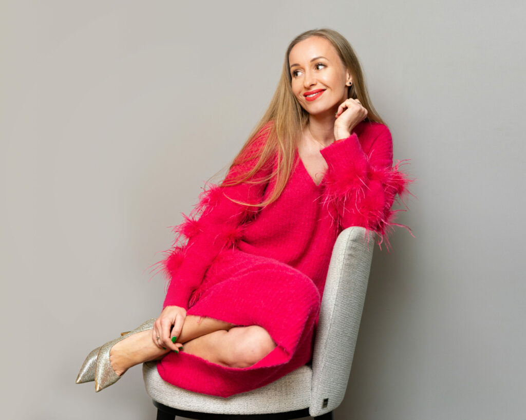 Stilberaterin Kashia Lehmann in einem pinken Strickkleid sitzend und lächelnd